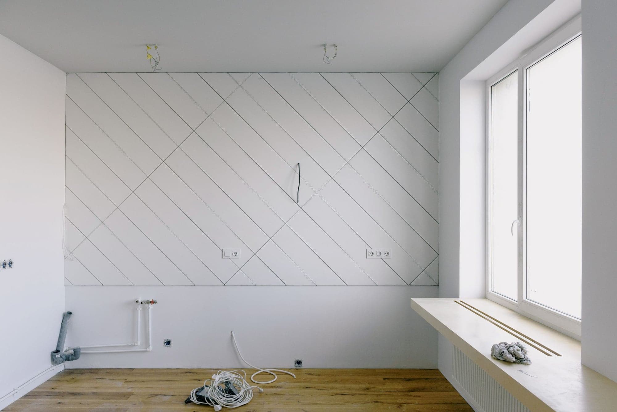 Avant : pièce en chantier, murs bruts tracés au crayon, câbles et tuyaux au sol.
