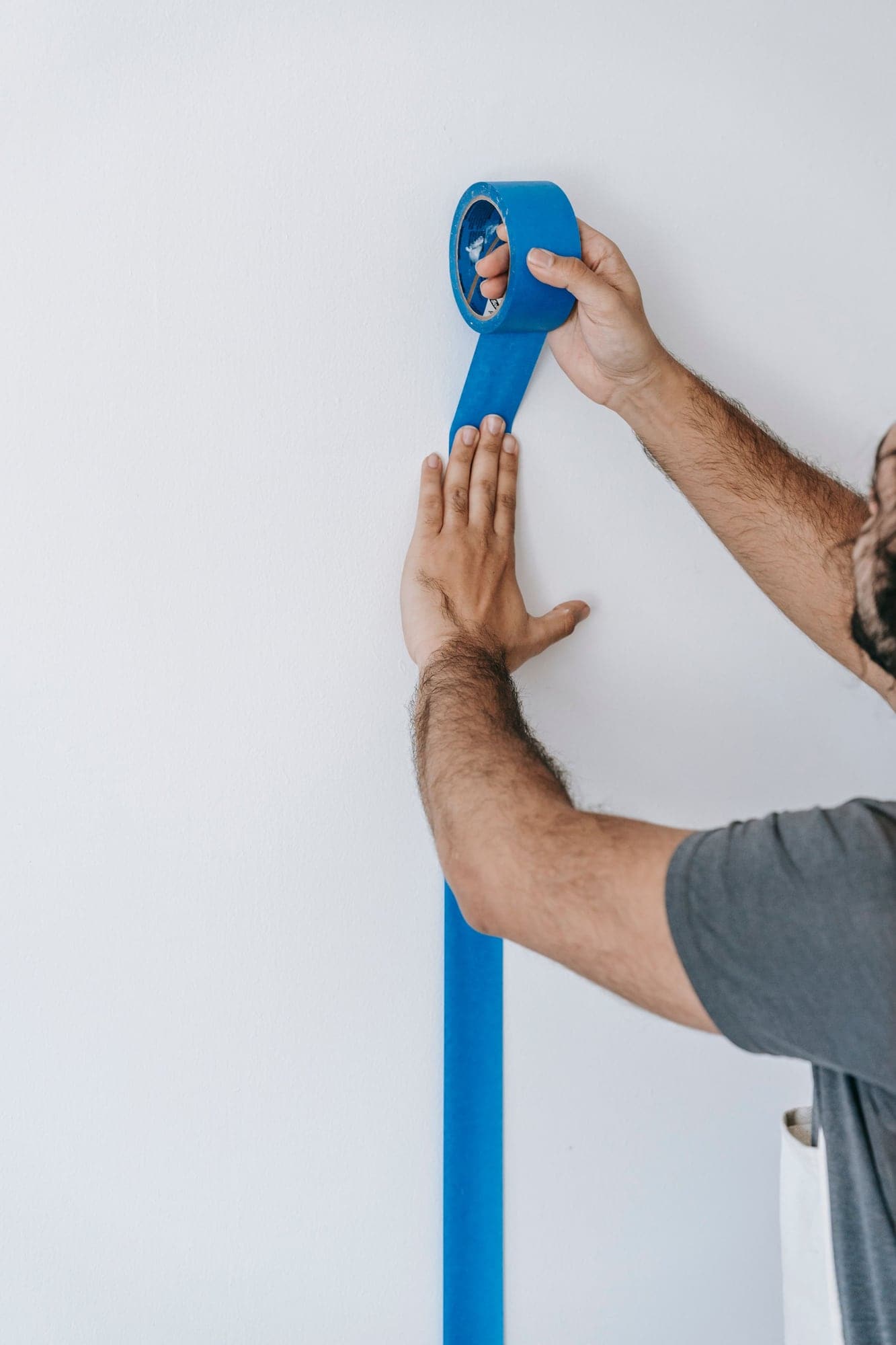Mains posant une bande de ruban de masquage bleu le long d’un angle de mur.
