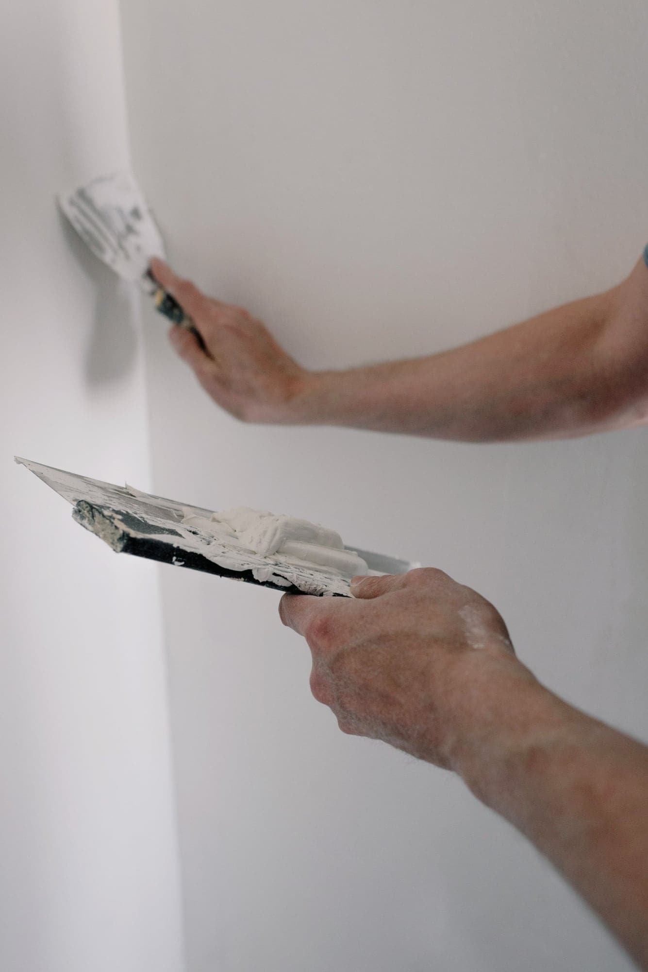 Mains tenant une spatule et une taloche pour lisser un mur blanc.