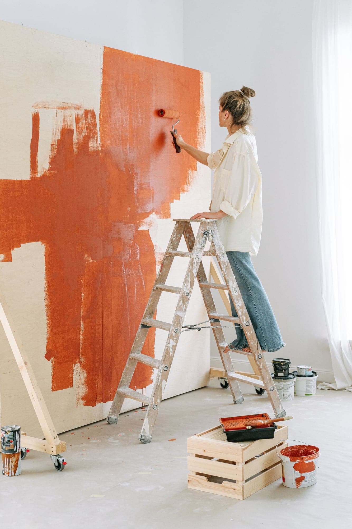 Mur blanc en cours de peinture en terre cuite, avec un escabeau et des pots de peinture.