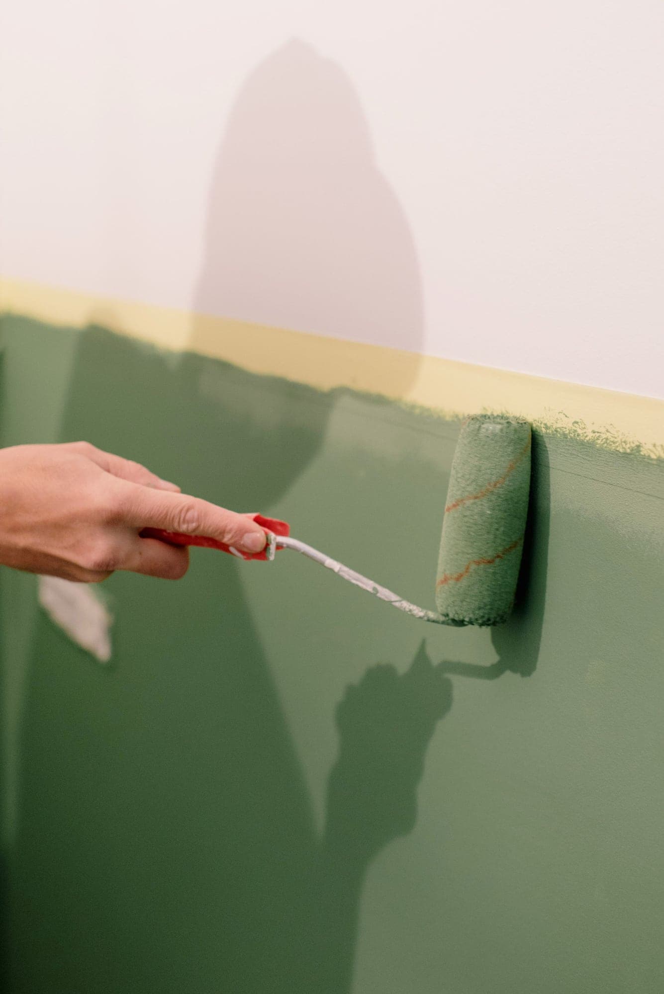 Rouleau appliquant une peinture vert sauge sous une ligne de soubassement bien droite.