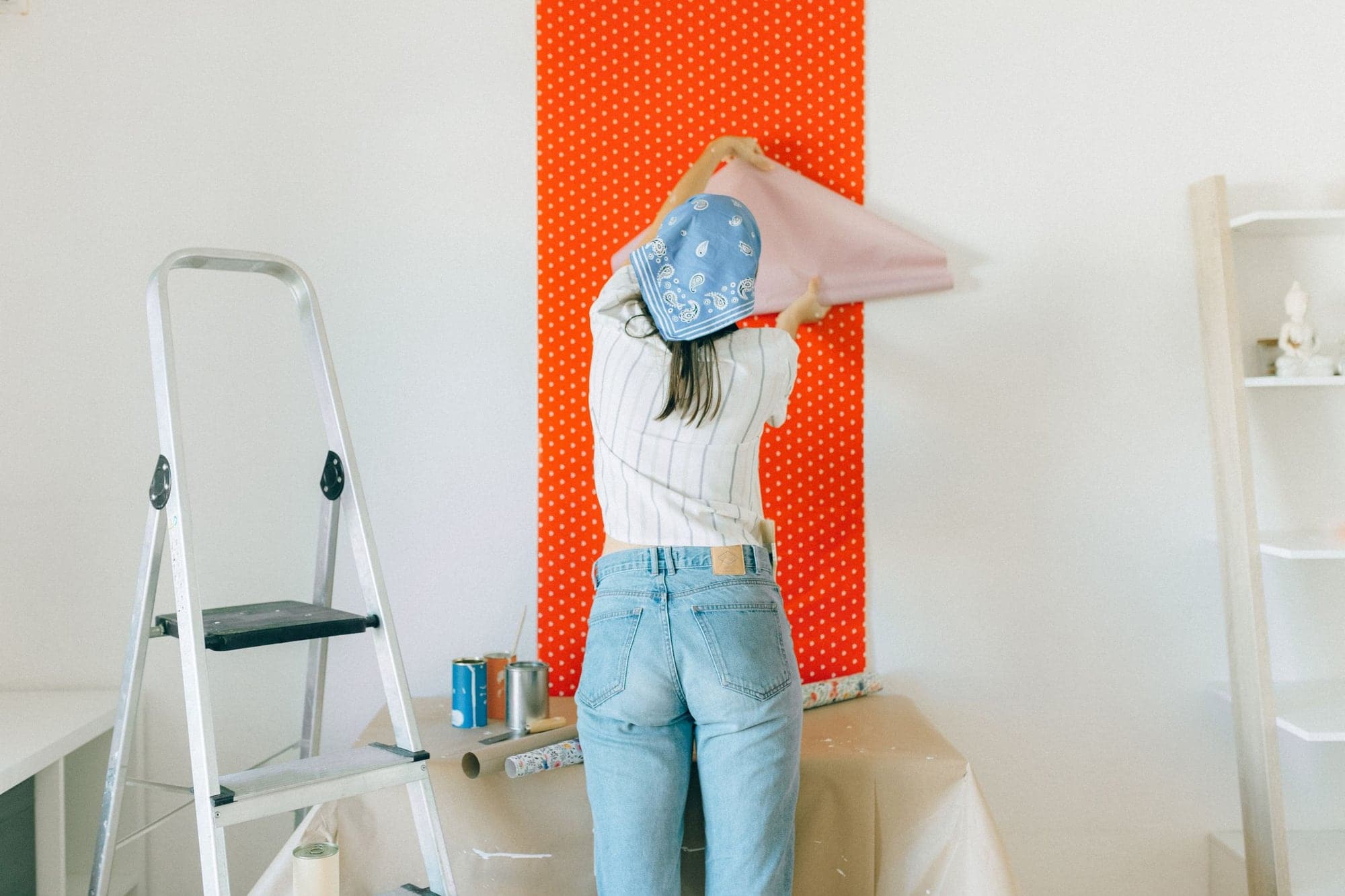 Pose d’un lé de papier peint à pois sur un mur blanc, avec un escabeau à côté.